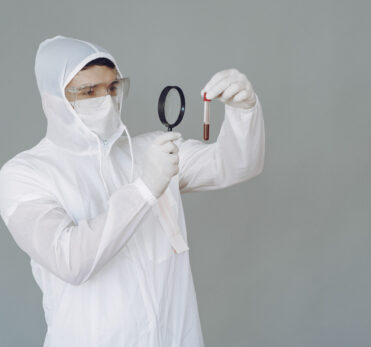 Corona virus theme. Man in a protective suit. Doctor looks at the blood tube.