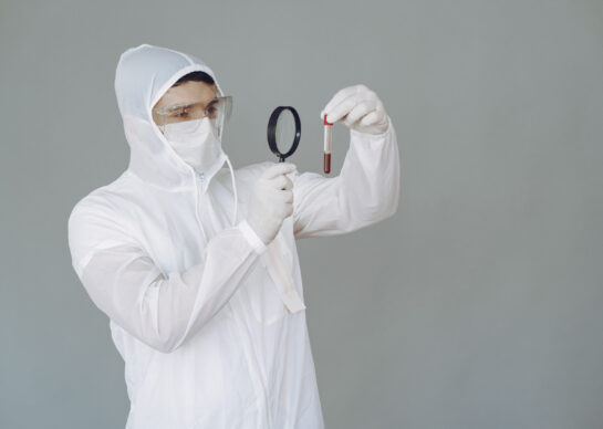Corona virus theme. Man in a protective suit. Doctor looks at the blood tube.
