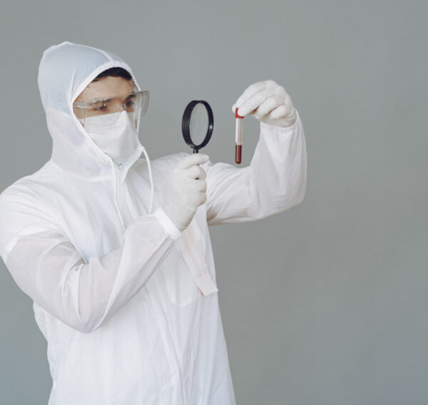Corona virus theme. Man in a protective suit. Doctor looks at the blood tube.