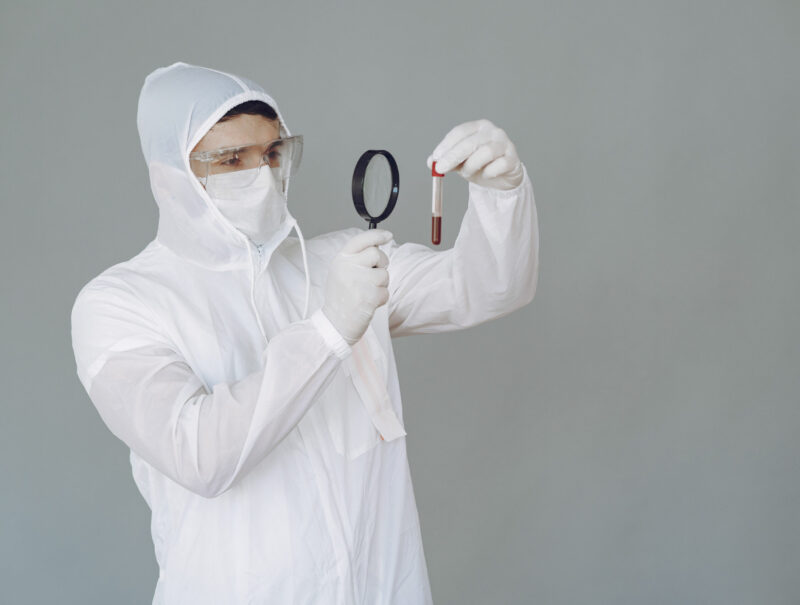 Corona virus theme. Man in a protective suit. Doctor looks at the blood tube.