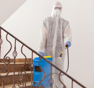 Man spreading disinfectant against covid-19 wearing biohazard costume.