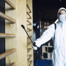Man in white protection suit disinfecting and fitness equipment and weights to stop spreading highly contagious corona virus.