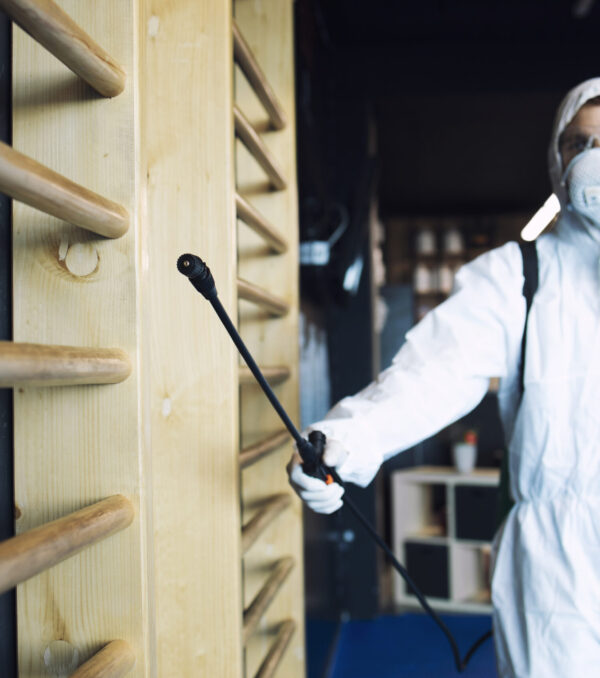 Man in white protection suit disinfecting and fitness equipment and weights to stop spreading highly contagious corona virus.