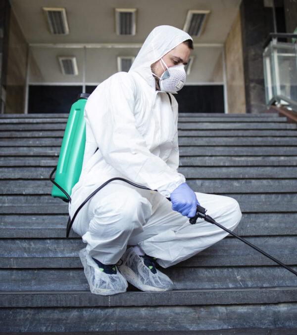 Person in white chemical protection suit disinfecting public corridors and steps to stop spreading highly contagious corona virus.