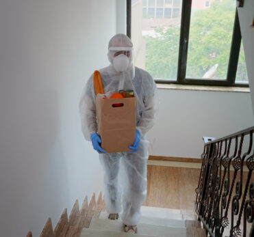 Volunteer delivering food order wearing coverall suit in covid-19 pandemic.