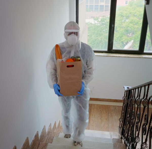 Volunteer delivering food order wearing coverall suit in covid-19 pandemic.