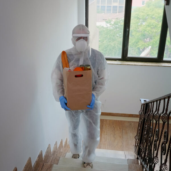 Volunteer delivering food order wearing coverall suit in covid-19 pandemic.